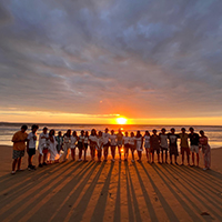Grupo mixto de jovenes en la playa con el sunset detrás